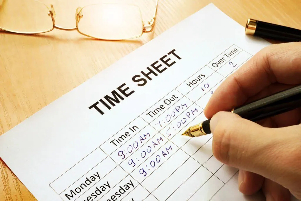 Hand filling in a paper time sheet with time in, time out and hours